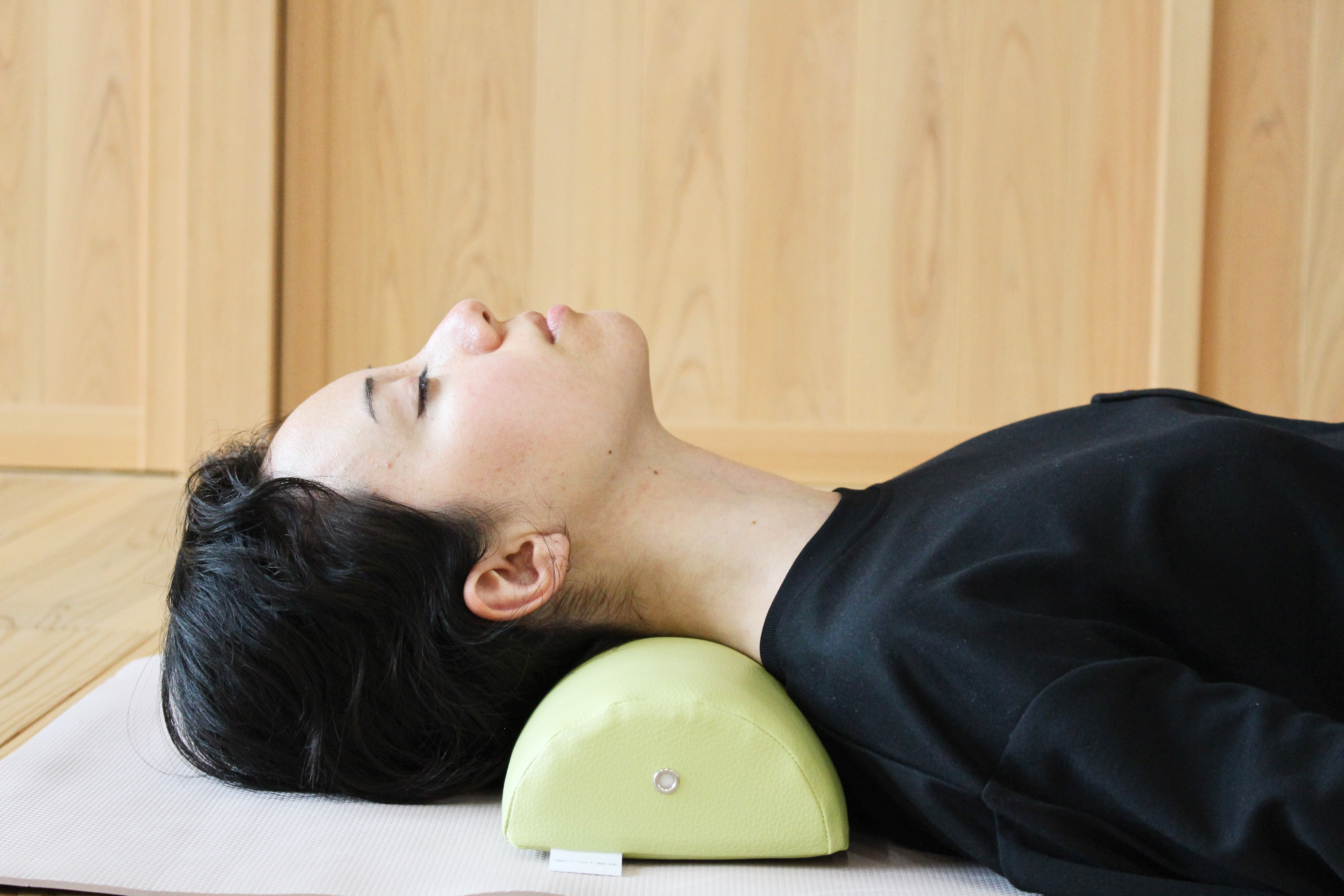 A woman demonstrates using the NeckEz pillow to restore natural neck curvature.