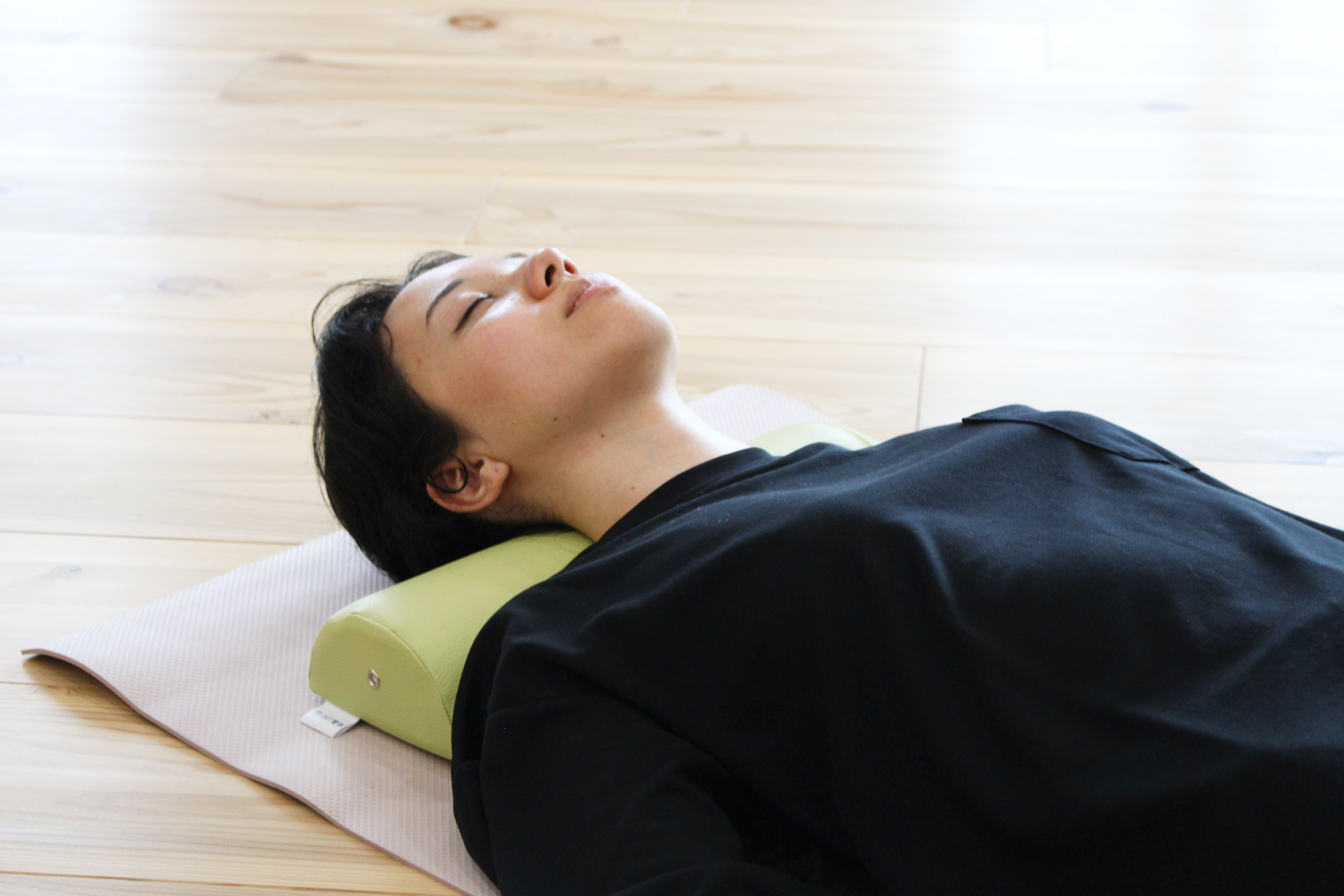 A woman demonstrates using the NeckEz Pillow to stretch her neck.
