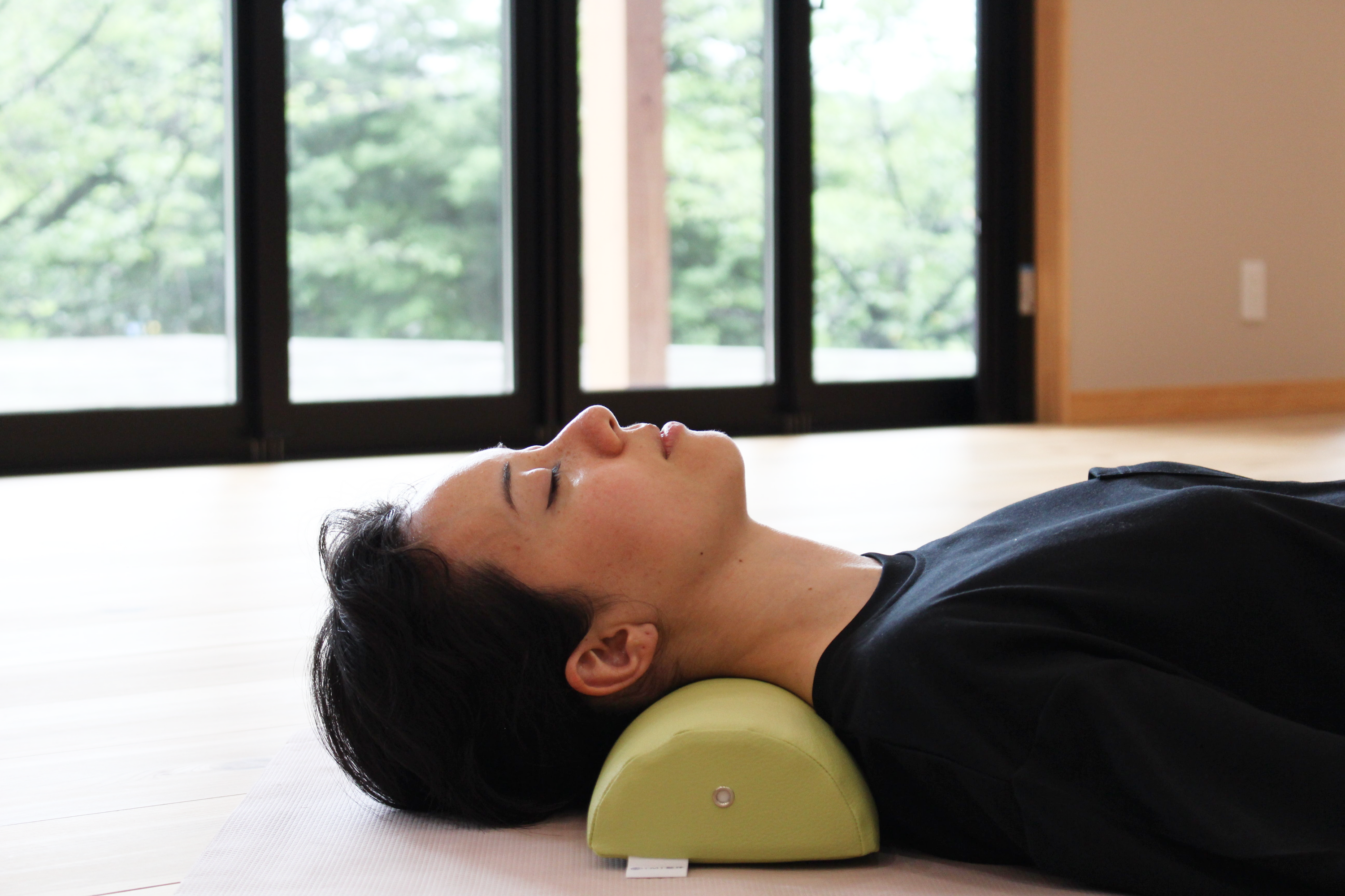 A woman demonstrates using the NeckEz Pillow to stretch her neck.