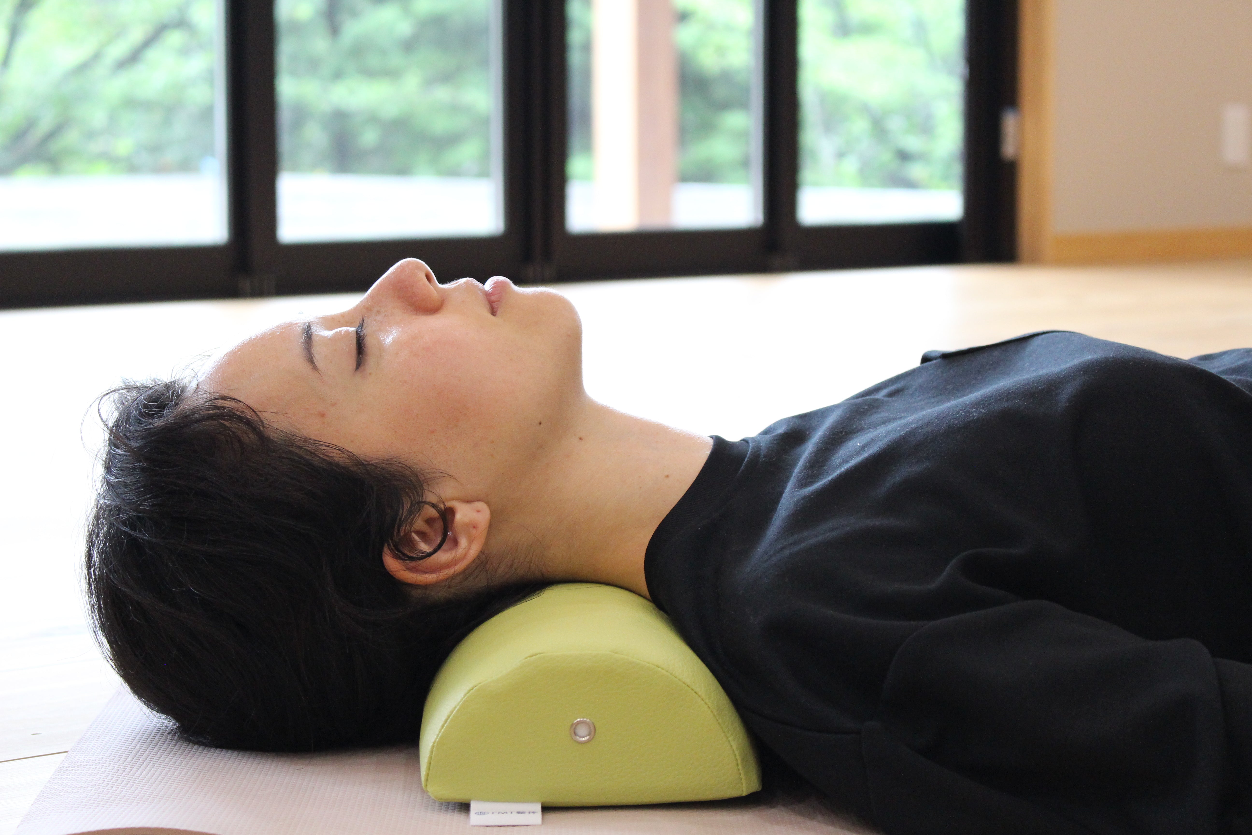 A woman demonstrates using the NeckEz Pillow to safely stretch her neck.