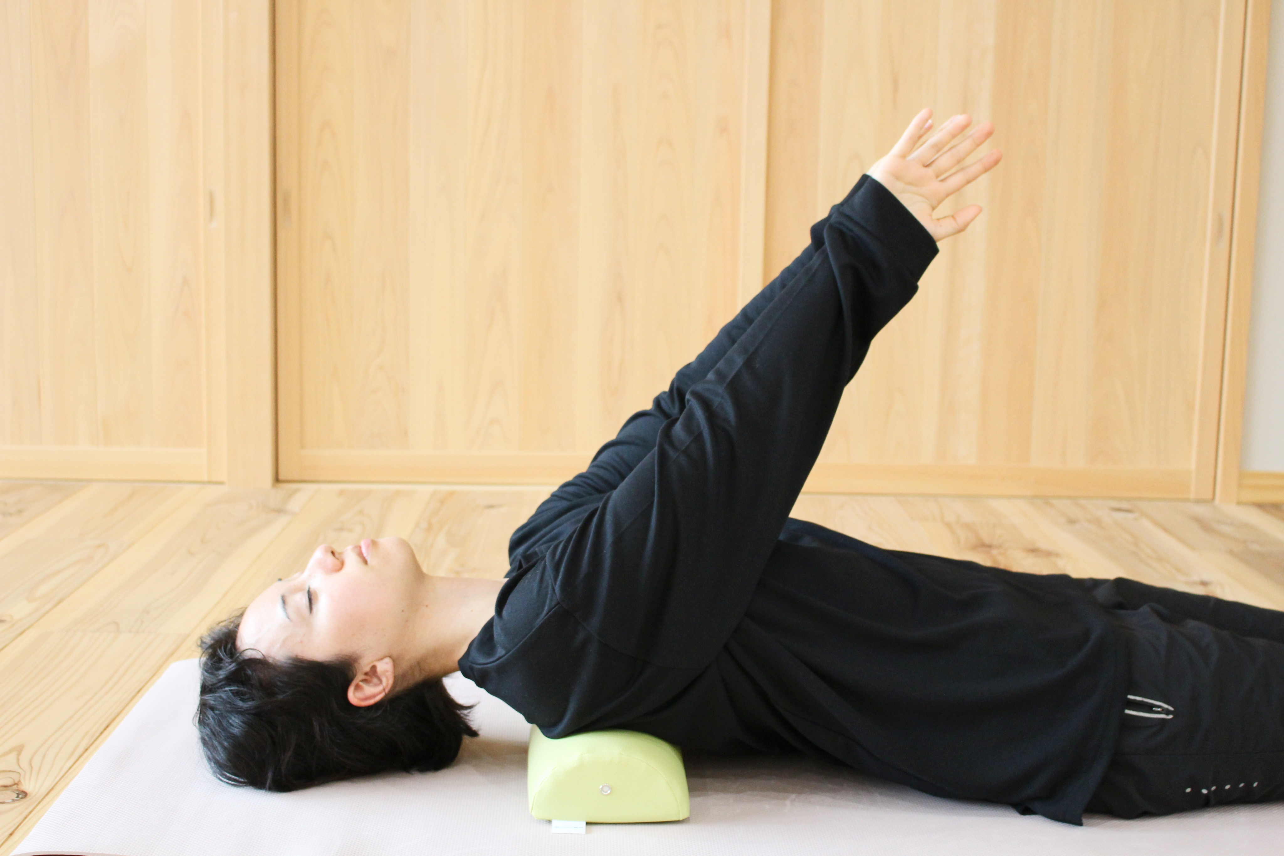 A woman demonstrates using the NeckEz Pillow to stretch her shoulders.